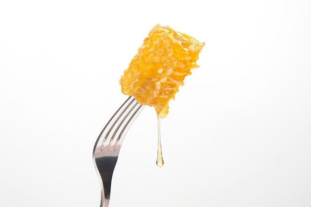 Drops of fresh honey drip from wax honey on a table fork