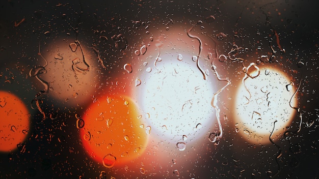 Drops of rain flow down the glass against the bokeh background of moving cars