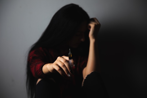 Drug addict sitting on the floor holding a syringe