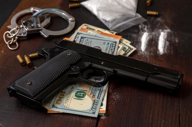 Drugs smuggling and trafficking Handcuffs pistol money and cocaine on wooden table background