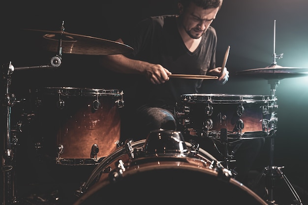 The drummer plays drums while sitting at the drum kit on stage.