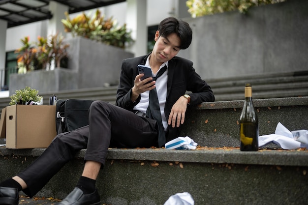 A drunk and hopeless Asian unemployed businessman is sitting on the stairs in front of the building