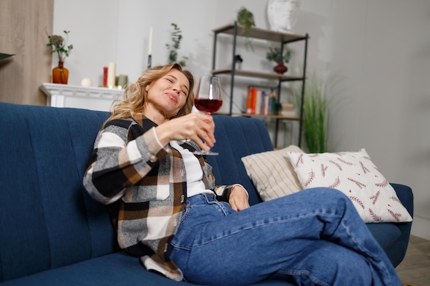 Drunk middleaged woman with glass of red wine on sofa at home