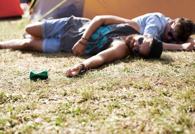 Drunk sleeping and men on camping ground at a music festival with alcohol Field drinking and lawn with a tent and youth on grass with people and man camper at concert outdoor with cans