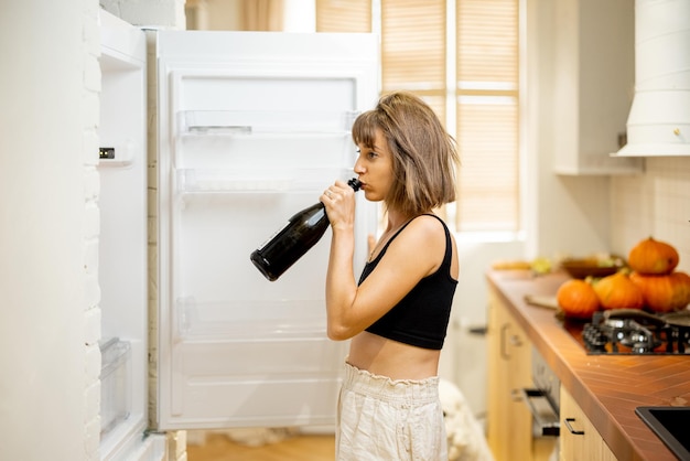 Drunk woman drink some alcohol near fridge at home