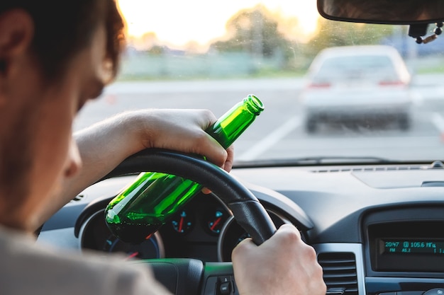 Drunk young man driving a car with a bottle of beer. Don't drink and drive concept