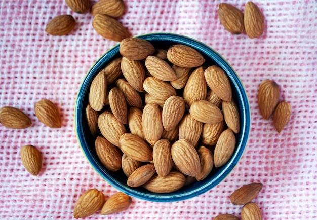 Dry almonds in a bowl next to another almonds on a pink surface.