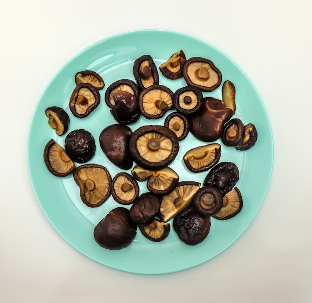 Dry and boiled champignon mushrooms in a plate on a white surface