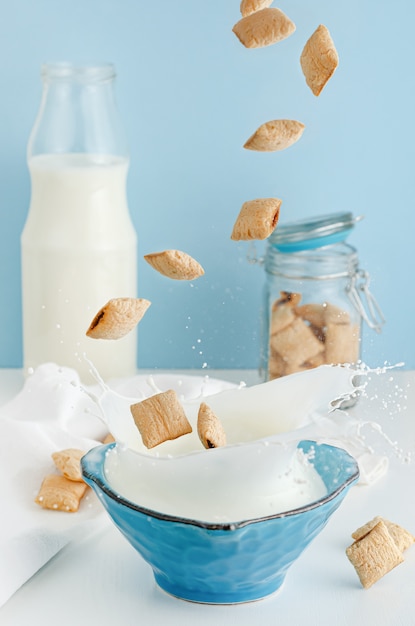 Dry breakfast of cereal corn pads with cocoa filling and blue bowl of organic milk. Levitation and flying food concept.