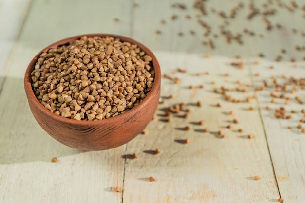 Dry buckwheat in brown clay bowl on wooden table. gluten free grain for healthy diet