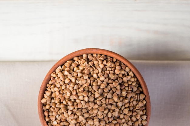 Dry buckwheat in brown clay bowl on wooden table. gluten free grain for healthy diet