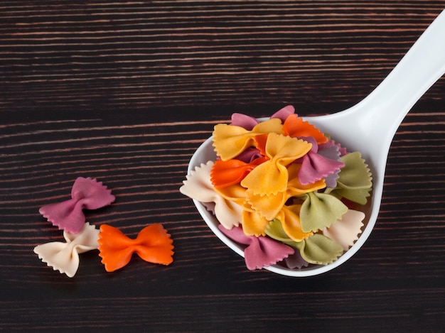 Dry colorful Italian pasta farfalle or bows in spoon on dark wooden background With copy space