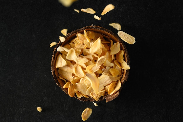 Dry flakes of garlic in a coconut bowl on a dark gray surface