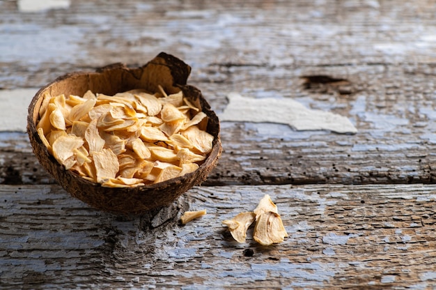 Dry garlic in flakes in a coconut bowl on an old wooden background