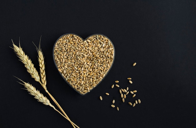 Dry grain of wheat in the form of a heart on the black background Top view Copy space