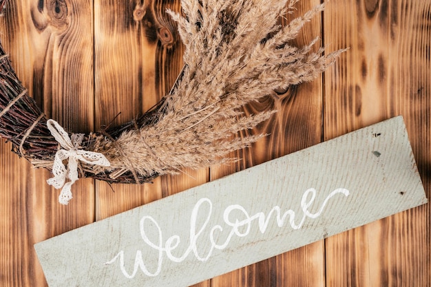 Dry herbal cereal tightly woven wreath with string and nameplate welcome Rustic brown wooden and planking door on background Celebration and preparation warm greeting of guests Cosy composition