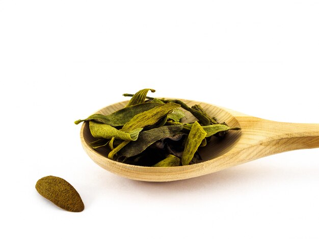 Dry mistletoe petals lie in a wooden spoon on a white 