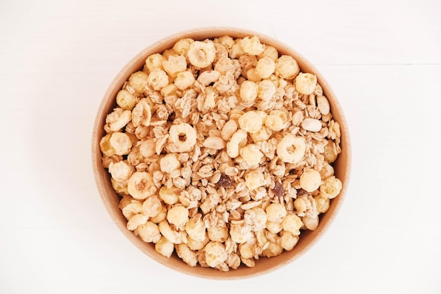 Dry muesli with cornflakes nuts and raisins in a wooden bowl on a white background