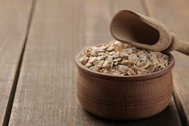 Dry oatmeal in a bowl and a wooden spoon on a brown wooden table