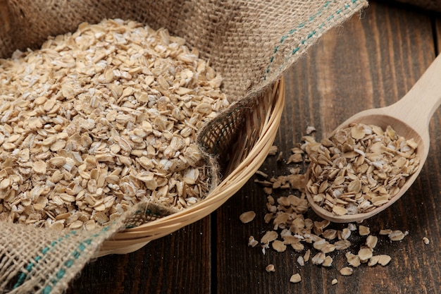 Dry oatmeal in a bowl and a wooden spoon on a brown wooden table 