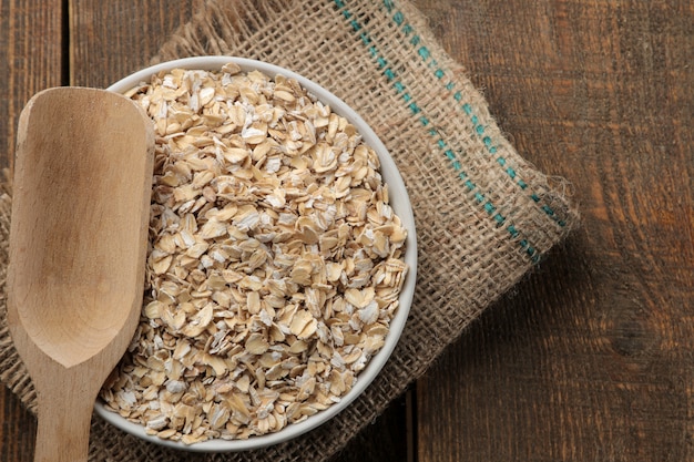 Dry oatmeal in a white bowl and a wooden spoon 