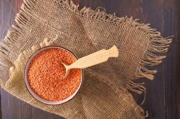 Dry orange lentils in a bowl on wooden background top view