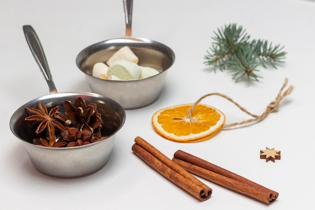 Dry orange on string cinnamon sticks sprig of spruce Marshmallow and star anise in metal bowls