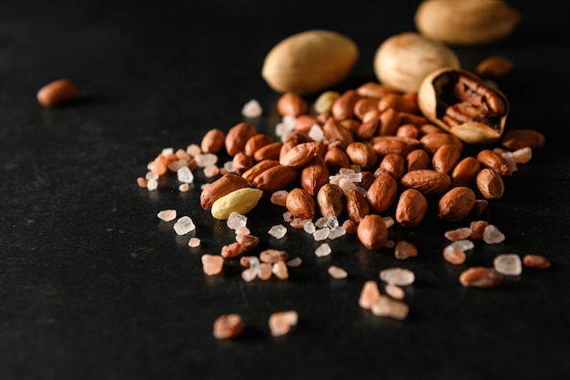 Dry peanuts with Himalayan coarse salt on a dark gray surface