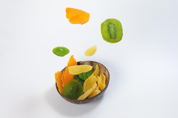 Dry preserved green kiwi pineapple ripe fruit slice colorful sweet on black marble slate background coconut shell bowl flying floating elevated drooping