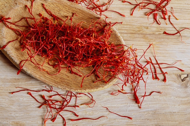 Dry saffron threads in a wooden spoon on a wooden background.