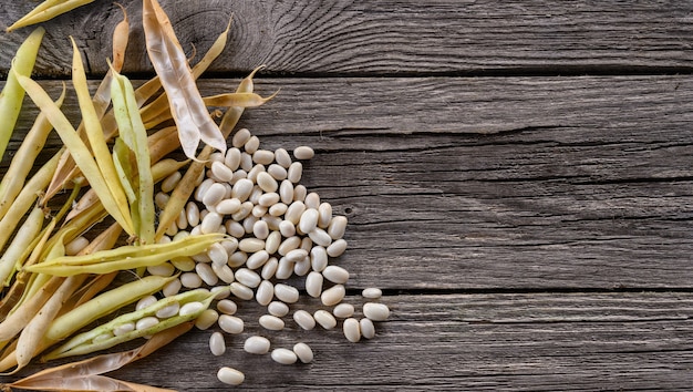 Dry string bean pods and white beans on old wooden table. Top view