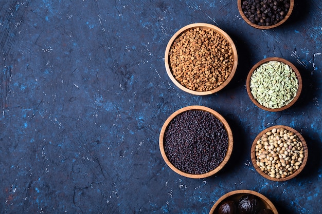 Dry whole Indian spices in wooden bowls on dark blue concrete rustic background. 