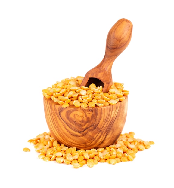 Dry yellow split peas in olive bowl and scoop, isolated on white background. Halves of yellow legume peas.