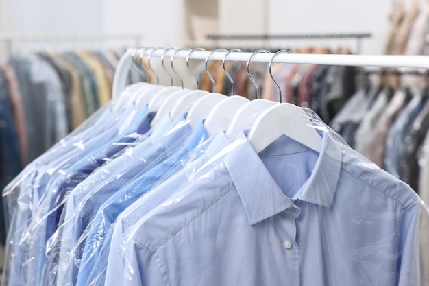 Photo drycleaning service many different clothes in plastic bags hanging on rack indoors closeup