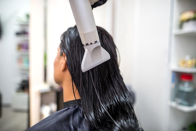 Drying long dark hair with a hairdryerprofessional hairdresser dries the hair of a client in the salon hairstyle beauty hair care fashion service