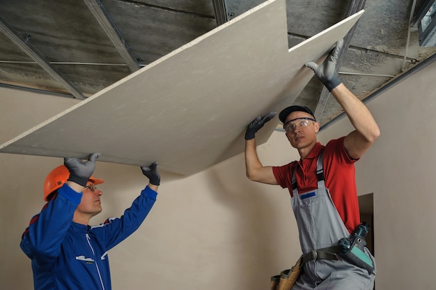 Drywall Installers. Men holding a gypsum board figured cut