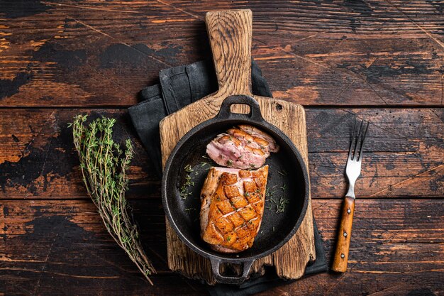 Duck breast roasted in a pan, poultry meat steak with herbs. Wooden background. Top view.