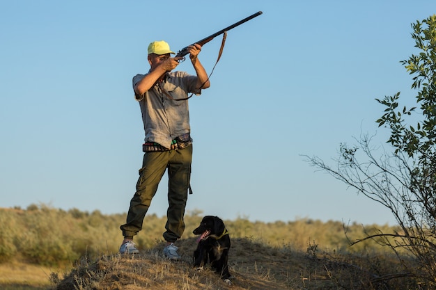 Duck hunter with shotgun walking through a meadow.