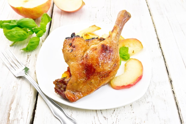 Duck leg with apple in plate on board