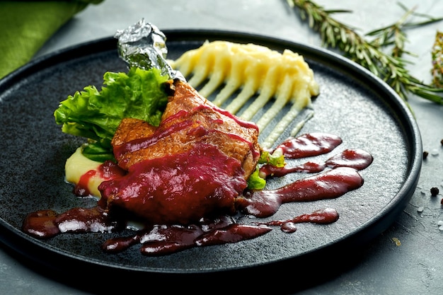 Duck leg with berry sauce and mashed potatoes on a black plate