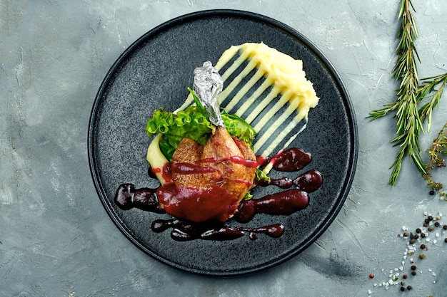 Duck leg with berry sauce and mashed potatoes on a black plate