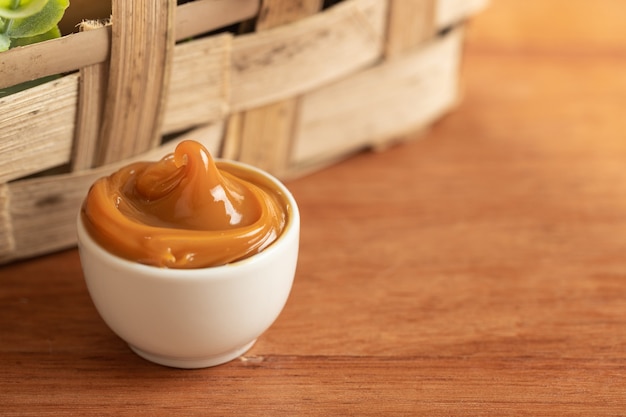 Dulce de leche in a white container on a wooden table.