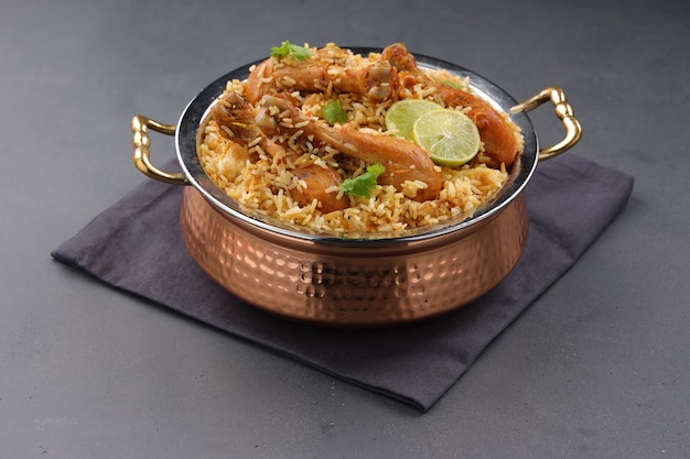 Dum chicken biriyani, close up image of Kerala-Thalassery biriyani  which is mixed with masala and yellow in colour arranged in a copper serving bowl and garnished with lemon slices  placed on graphit