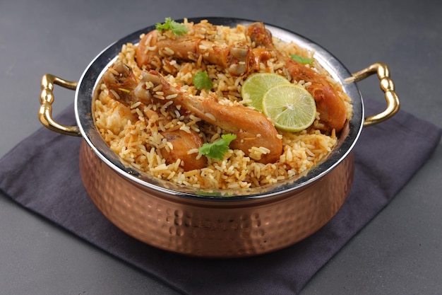 Dum chicken biriyani, close up image of Kerala-Thalassery biriyani  which is mixed with masala and yellow in colour arranged in a copper serving bowl and garnished with lemon slices  placed on graphit