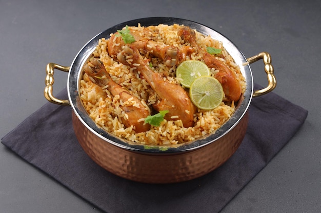 Dum chicken biriyani, close up image of Kerala-Thalassery biriyani  which is mixed with masala and yellow in colour arranged in a copper serving bowl and garnished with lemon slices  placed on graphit