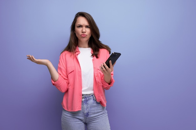 Dumb brunette woman in informal look with mobile phone on studio background