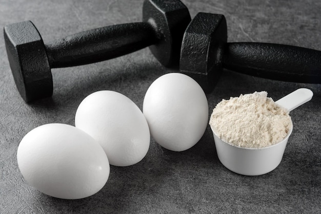 Dumbbells protein scoop and chicken eggs closeup on a dark background