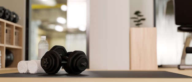 Dumbbells towels and a bottle of water on a exercise mat over blurred modern fitness gym