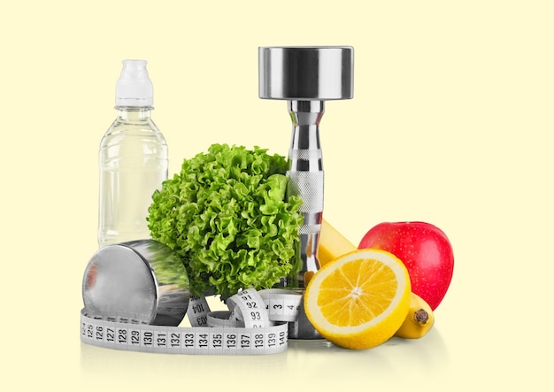 Dumbbells with measuring tape and fruits on light background