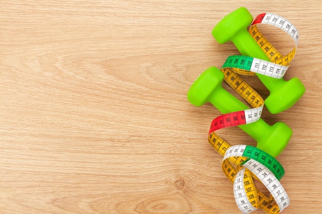 Dumbells and tape measure over wooden table with copy space